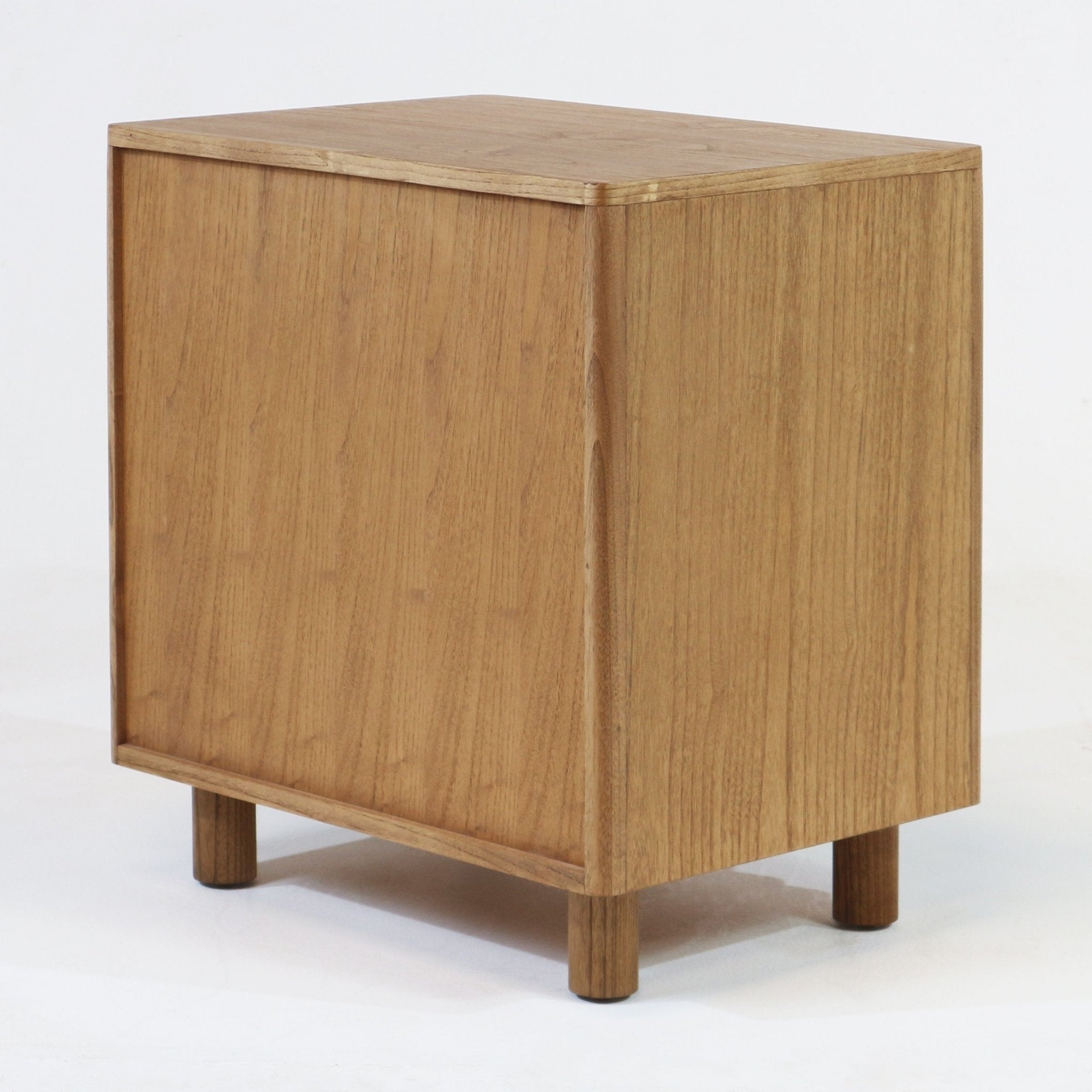 Light blonde solid wood nightstand shown at a corner angle, minimalist Scandinavian cube design with rounded edges, visible oak grain and four short cylindrical legs supporting the piece.