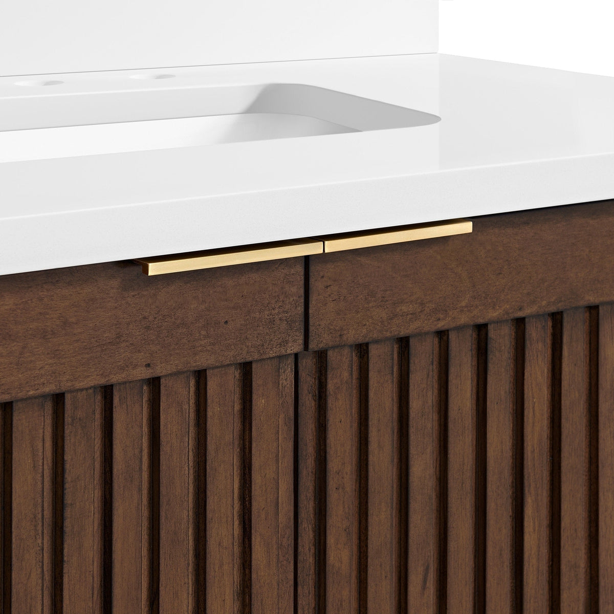 Close-up of a bathroom vanity showing a white stone countertop with integrated rectangular sink, fluted solid wood brown cabinet front and slim gold drawer handles.