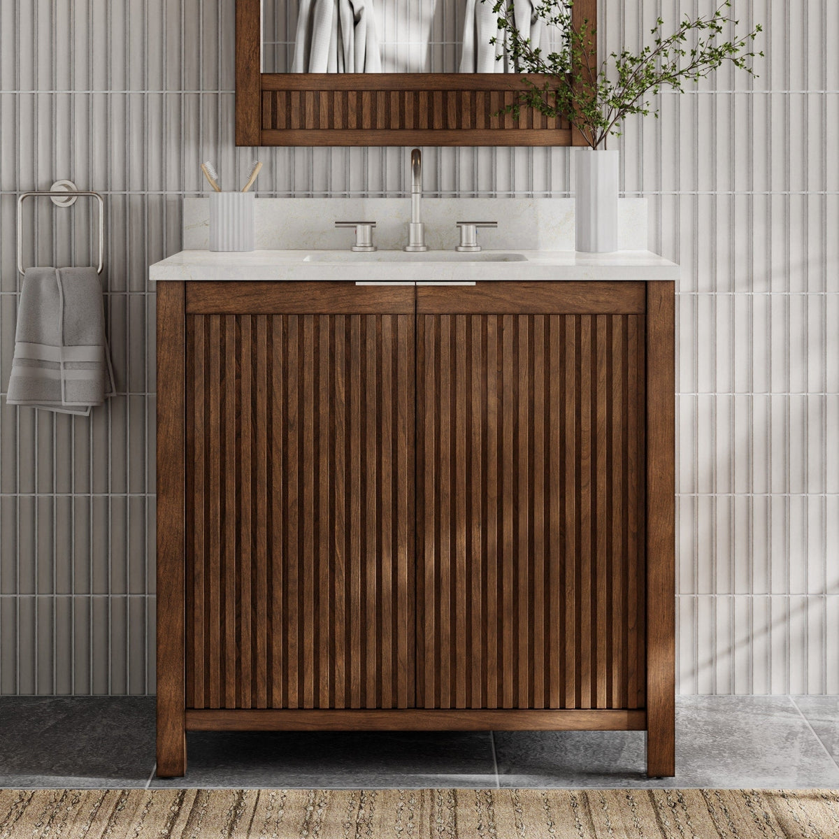 Front view of a modern solid wood single-sink bathroom vanity in warm brown with vertical fluted doors, stone countertop and integrated sink, brushed nickel faucet, wood-framed mirror, towel ring and white vase with greenery.