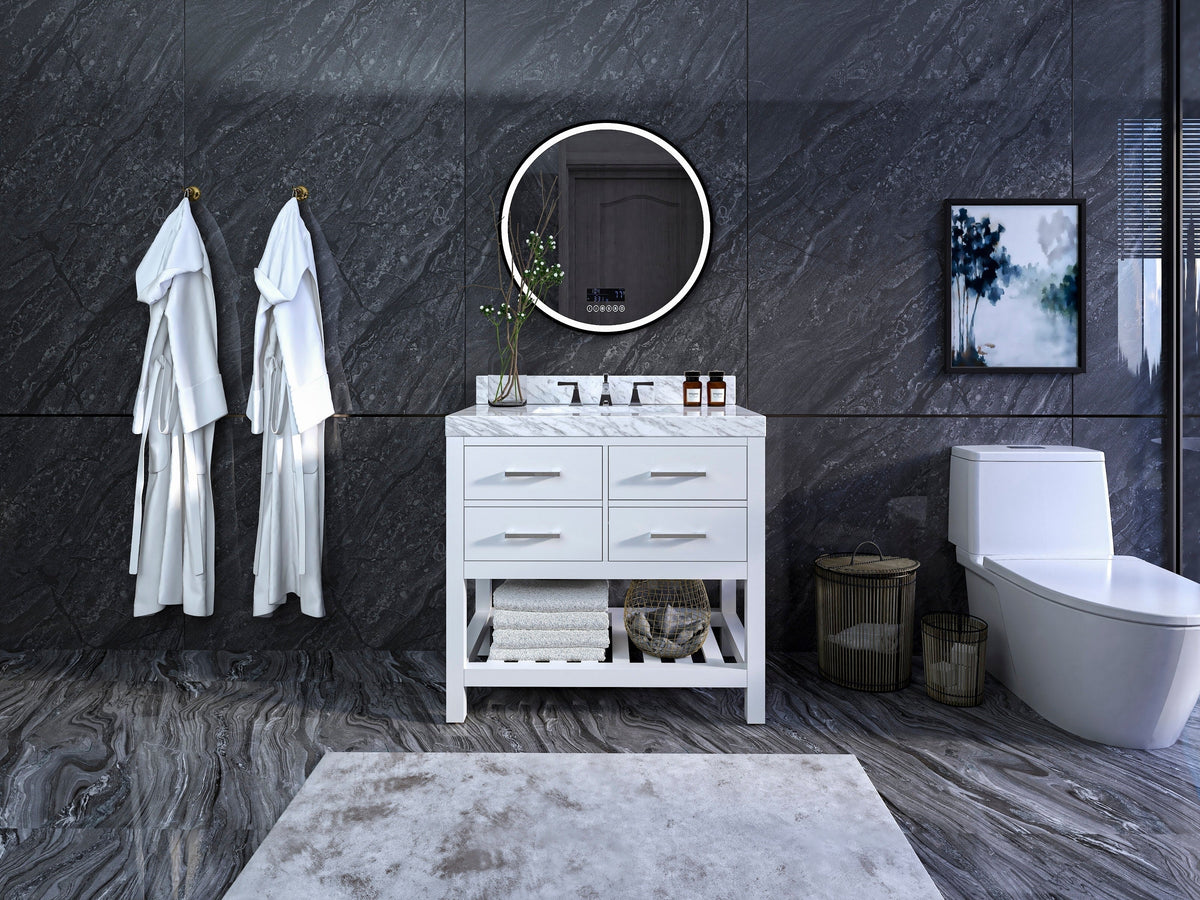 Modern freestanding white solid wood 36-inch single-sink bathroom vanity with stone top, four drawers and open shelf with towels, chrome faucet and round illuminated mirror against a dark stone wall.