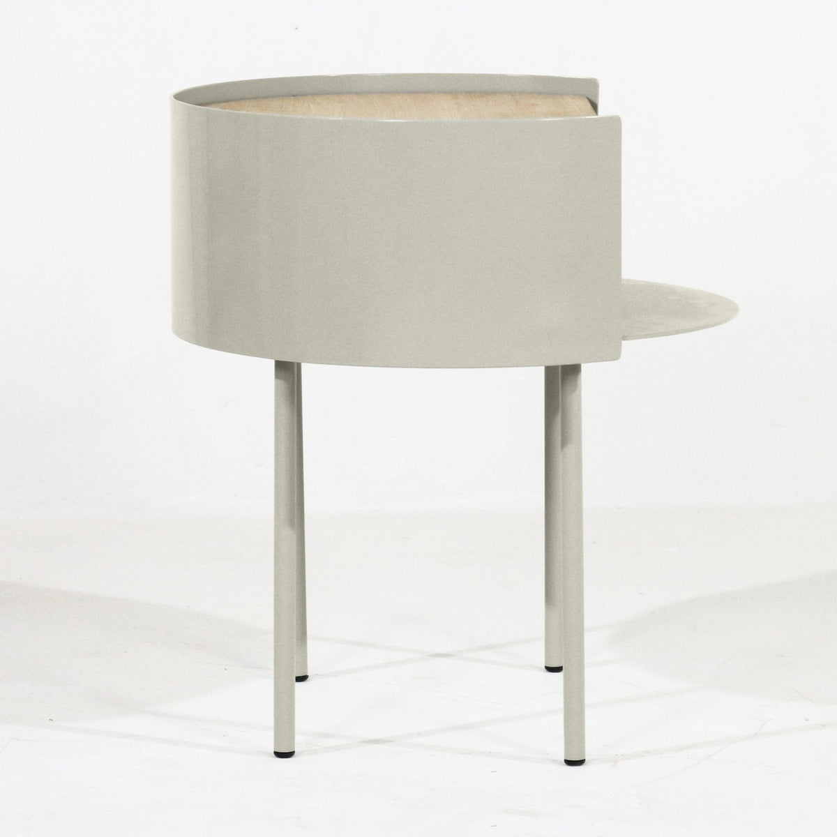 Modern nightstand featuring a curved light gray steel shell with a white oak top visible through the opening, three slim steel legs and a small round side shelf.