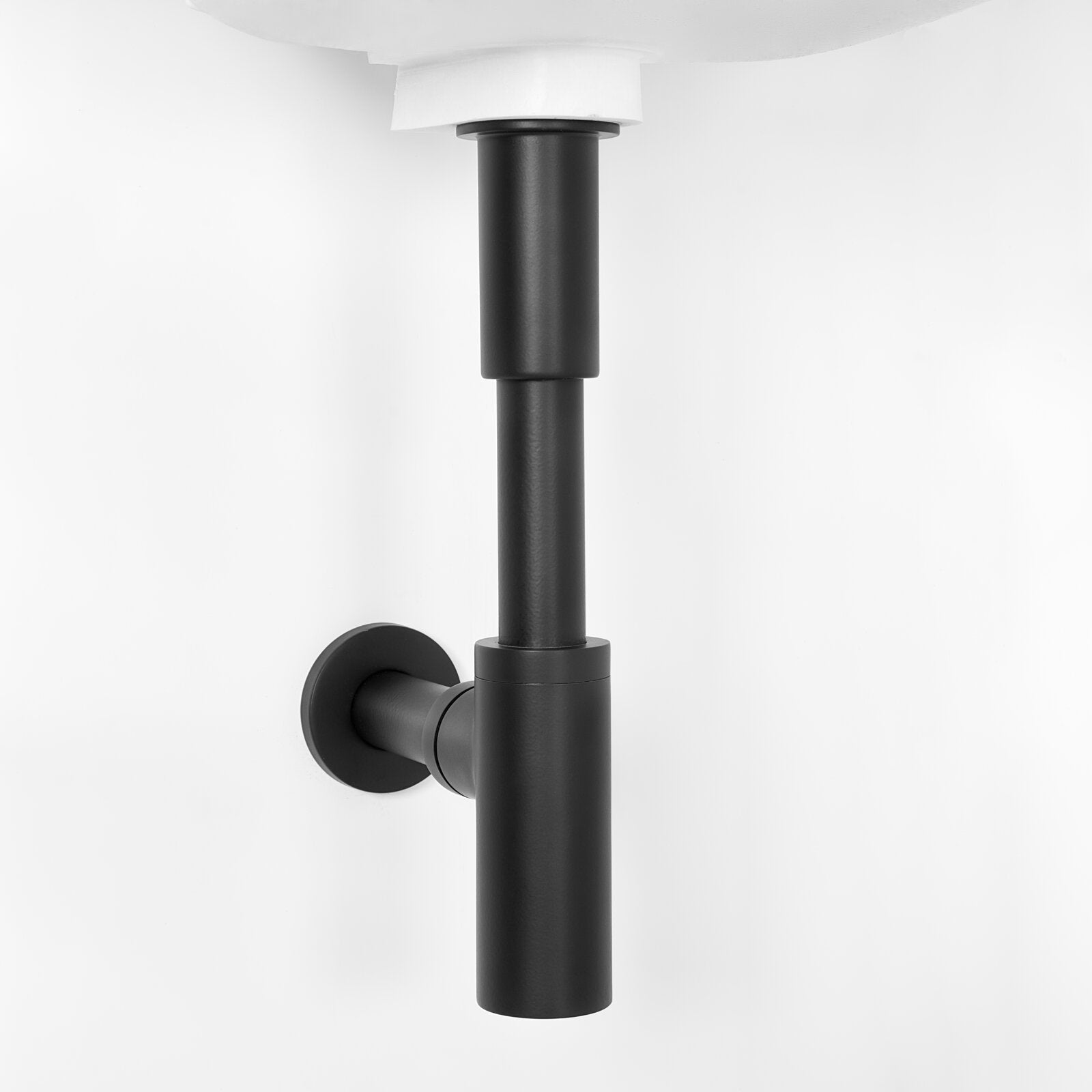 Close-up of a matte black metal bottle trap and wall flange installed beneath a white ceramic sink, highlighting cylindrical modern plumbing detail for a contemporary bathroom vanity.