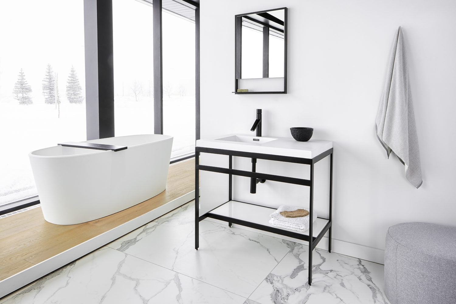Modern single-sink bathroom vanity with a white stone top and integrated rectangular sink, supported by a black metal open-frame base with matte black faucet; mirror above, freestanding white tub on wood platform and gray towel.
