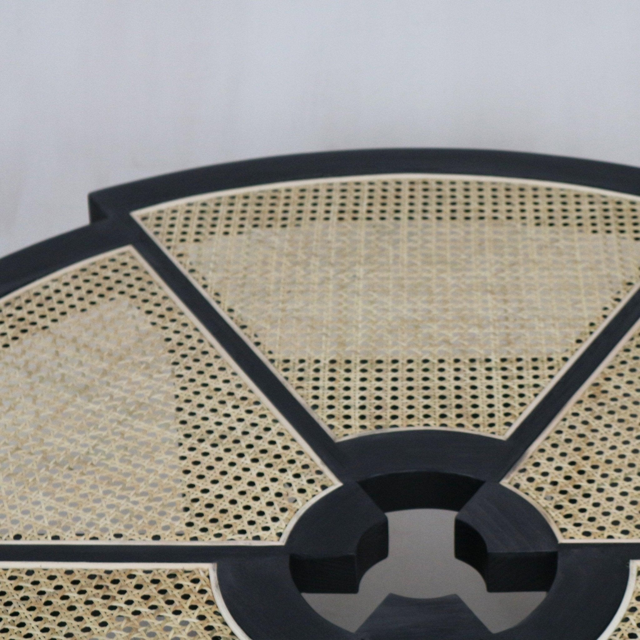 Close-up of a round coffee table top with natural cane weave panels set into a black wooden frame, showing the segmented radial pattern and circular center detail.