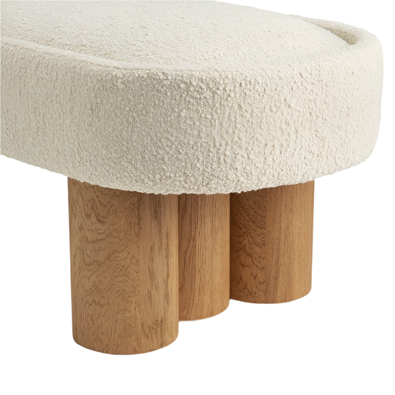 Close-up of a natural cream boucle-upholstered end-of-bed bench cushion showing textured boucle fabric and three rounded solid wood cylinder legs in a warm natural finish.