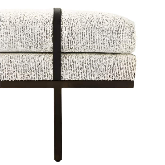 Close-up of the bench end showing natural boucle upholstery on layered cushions, a contrasting dark vertical strap, and a dark wood T-leg supporting the upholstered end-of-bed bench.