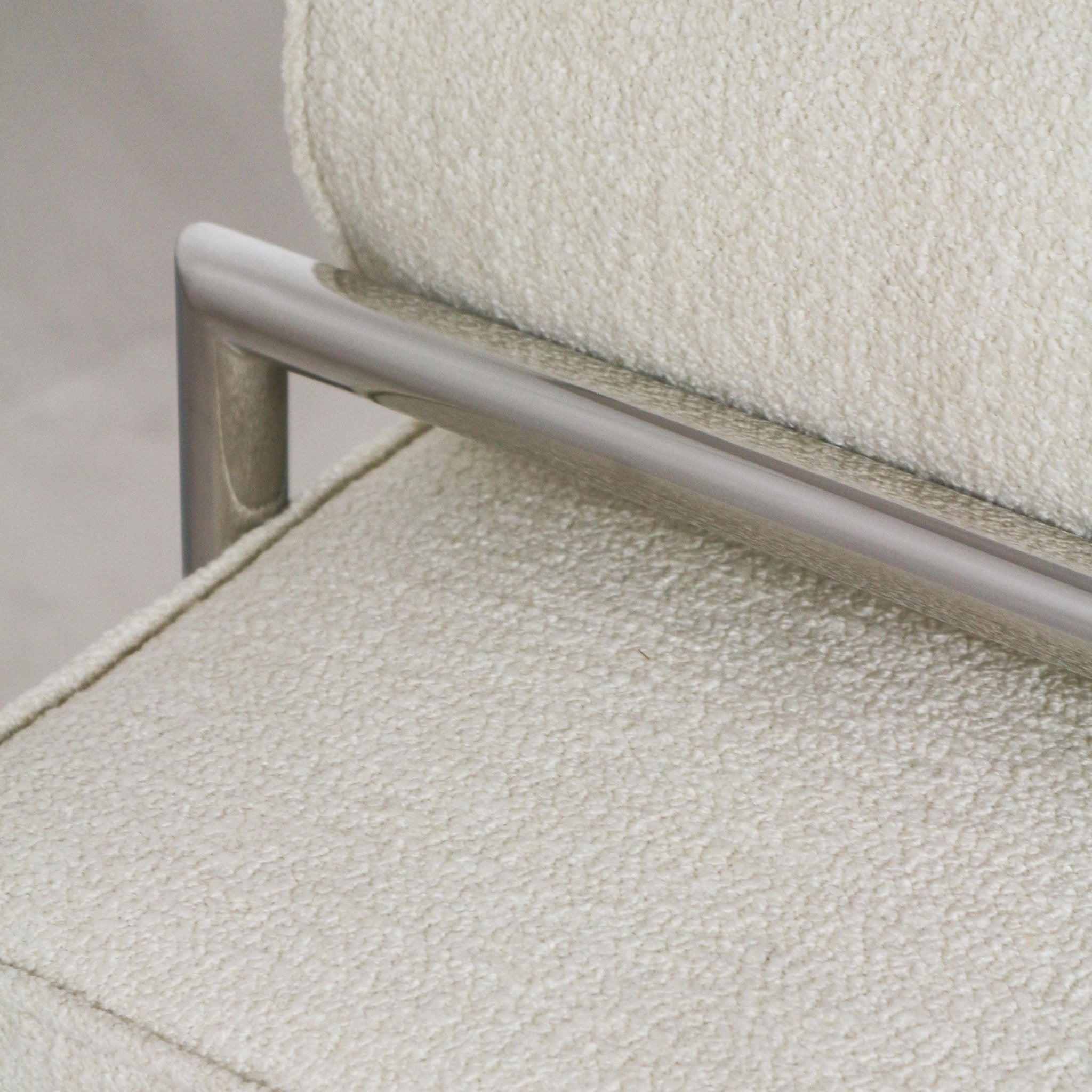 Close-up of an ivory boucle upholstered bench seat and back showing textured looped fabric and a slim brushed stainless steel frame with horizontal rail detail.