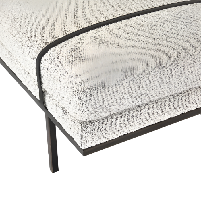 Close-up of a natural boucle-upholstered bench corner showing cream textured fabric, contrasting dark piping, layered cushion detail and a slim dark frame and leg.