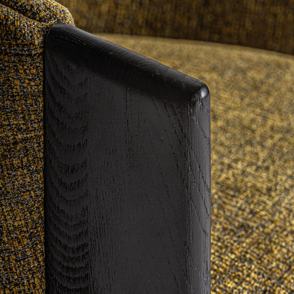 Close-up of a black-inked oak armrest on a dining chair beside mustard-yellow textured performance fabric upholstery, highlighting the wood grain and rounded edge.