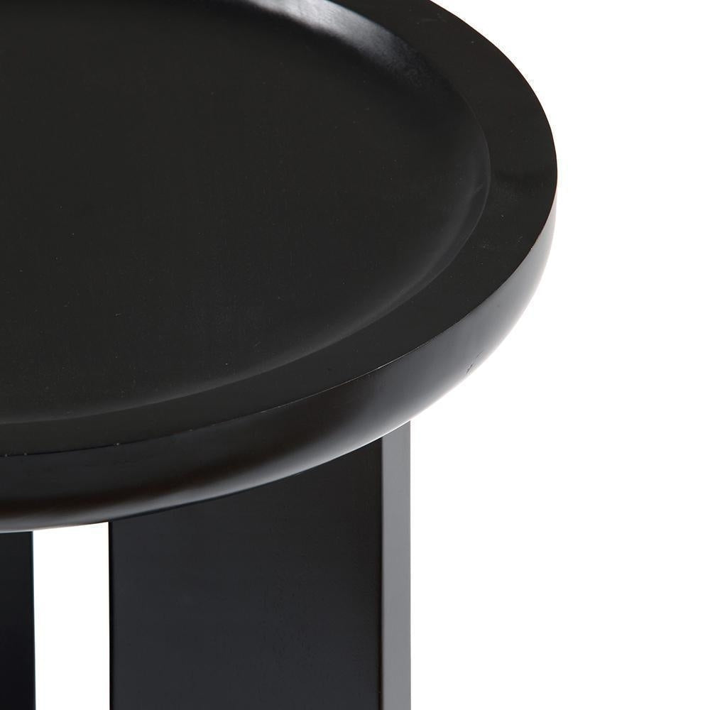 Close-up of a round black mahogany side table top with a shallow recessed center and two straight black wooden legs, highlighting the smooth finished edge and modern solid-wood construction.