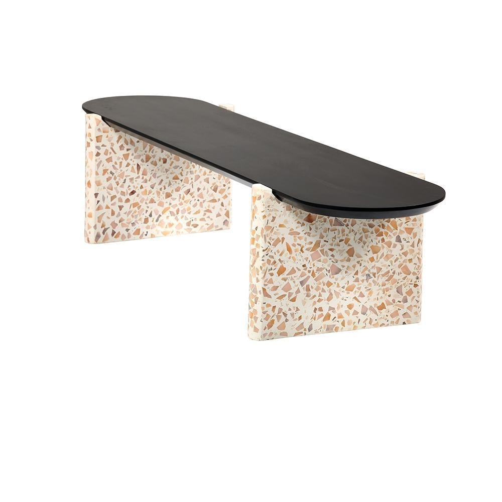 Modern coffee table with a long black wooden oval top supported by two cream terrazzo slab bases patterned with beige and brown stone chips.