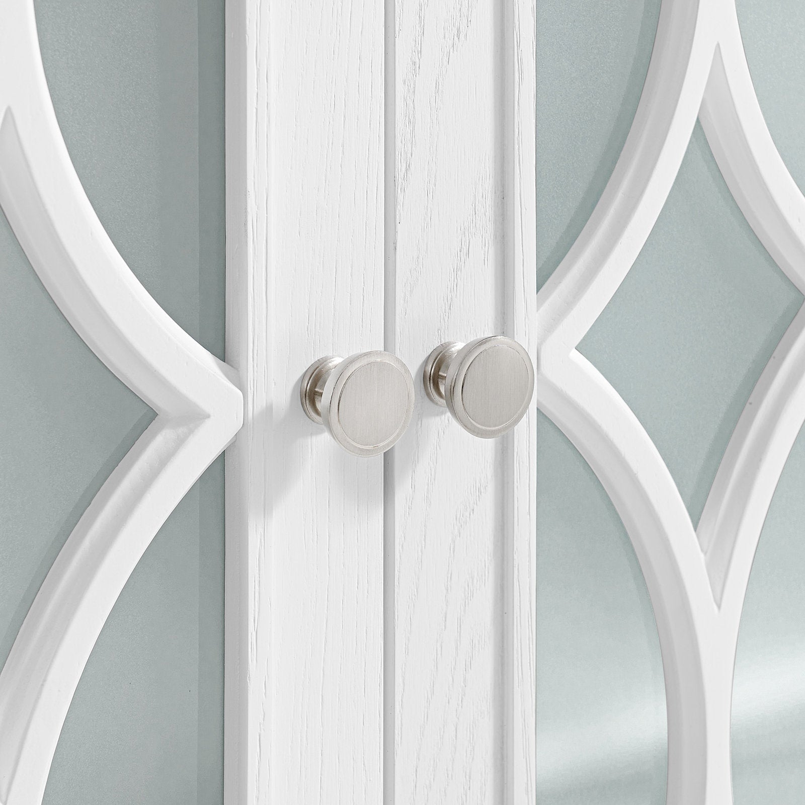 Close-up of a white solid-wood vanity door with a center seam, two round satin-nickel knobs and decorative white overlay framing stone-tinted glass panels.