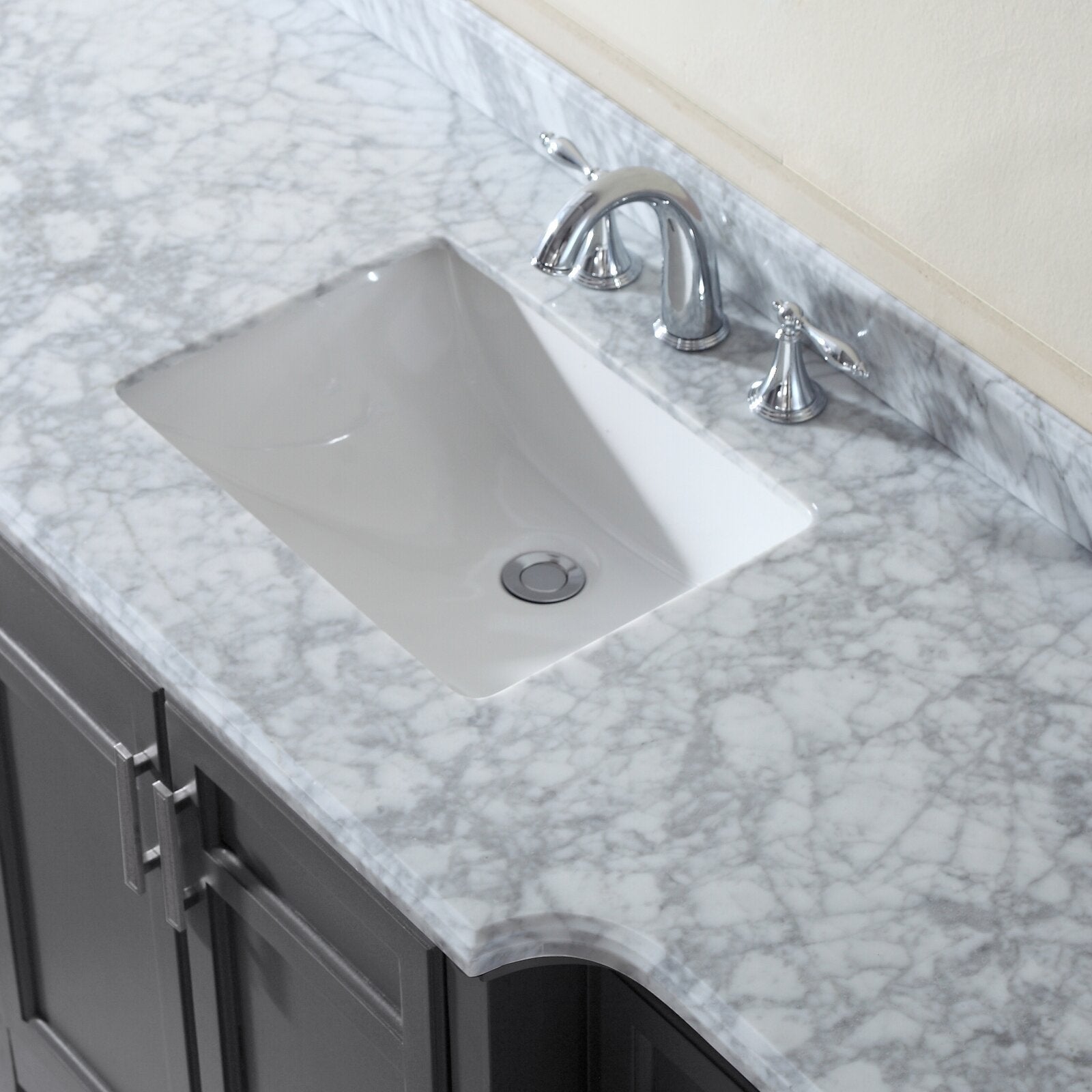 Close-up of a stone marble countertop with a rectangular white undermount ceramic sink, chrome widespread faucet, and gray solid wood vanity cabinets.