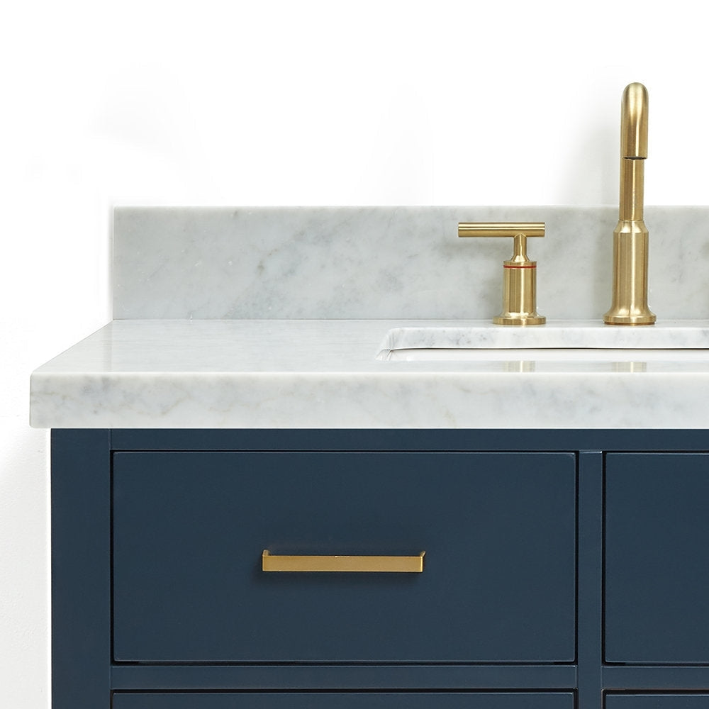 Close-up of a navy solid wood bathroom vanity with a light stone countertop and integrated rectangular ceramic sink, featuring a brushed brass faucet and matching brass drawer pull.