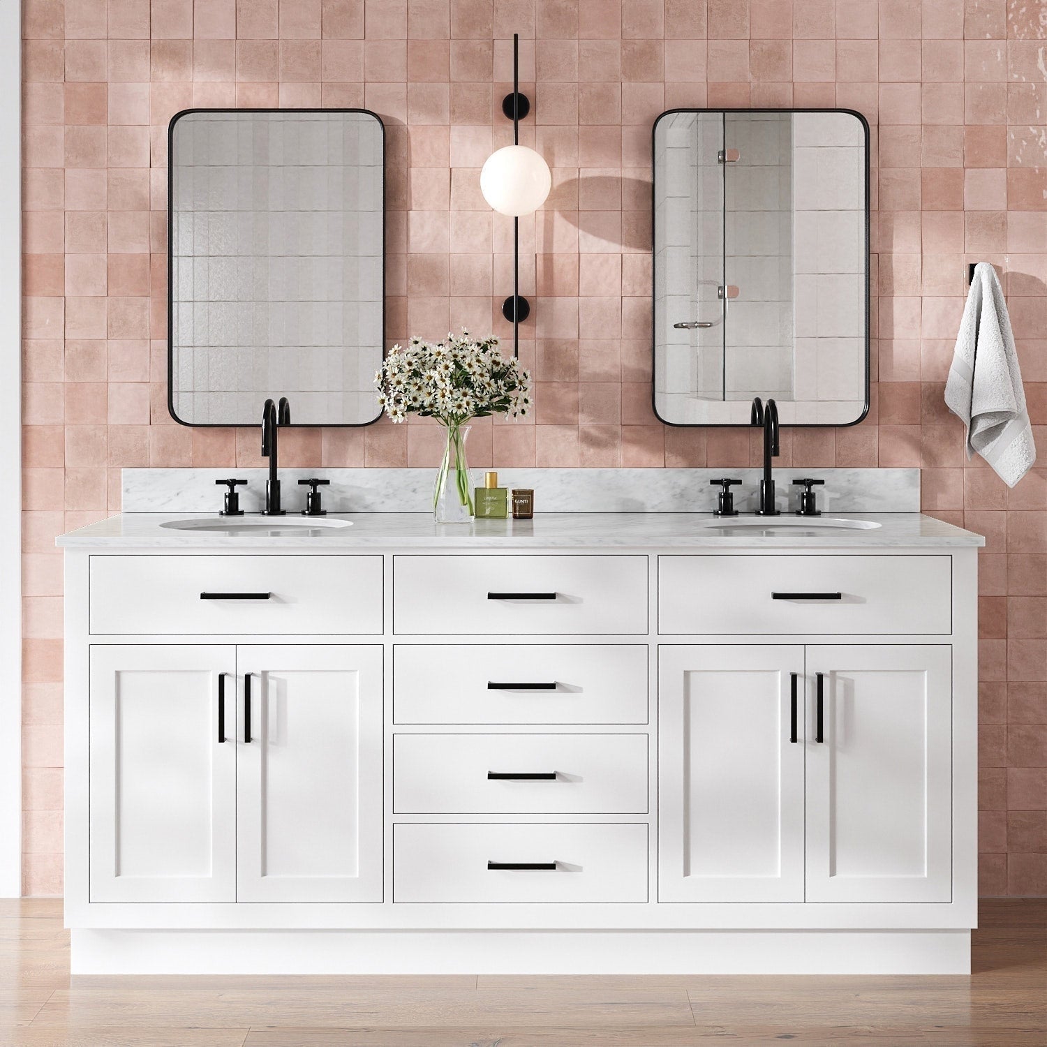Front view of a modern solid wood white vanity with white quartz top, two undermount sinks, matte black faucets and hardware, black-framed mirrors, and a vase of daisies against a pink tiled wall.