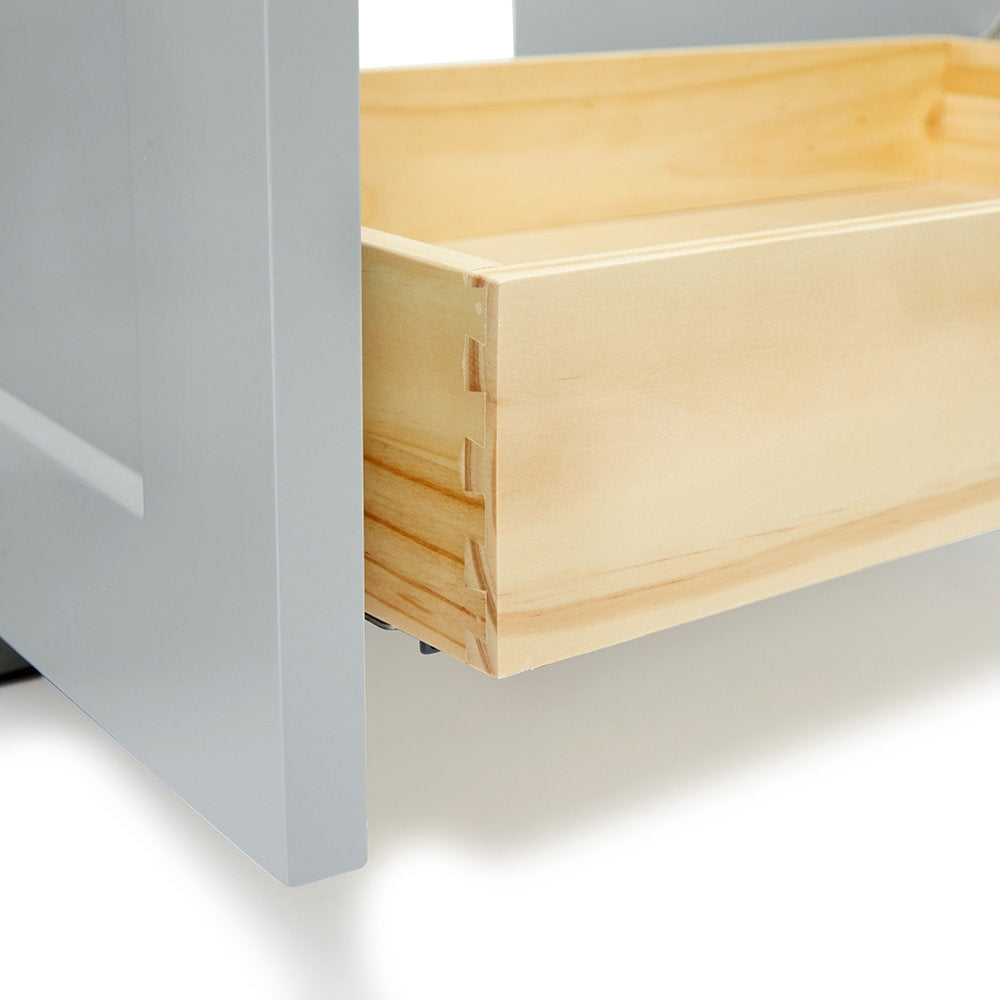 Close-up of a natural solid wood vanity drawer showing dovetail joinery and light wood interior, paired with a gray-painted cabinet side and a visible metal drawer slide.