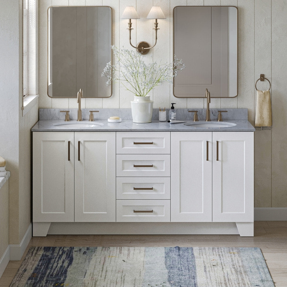 Modern solid-wood 73-inch double-sink bathroom vanity with gray stone countertop, white shaker cabinets and central drawers, satin bronze faucets and hardware, two rectangular mirrors, wall sconce and ceramic vase with flowers.