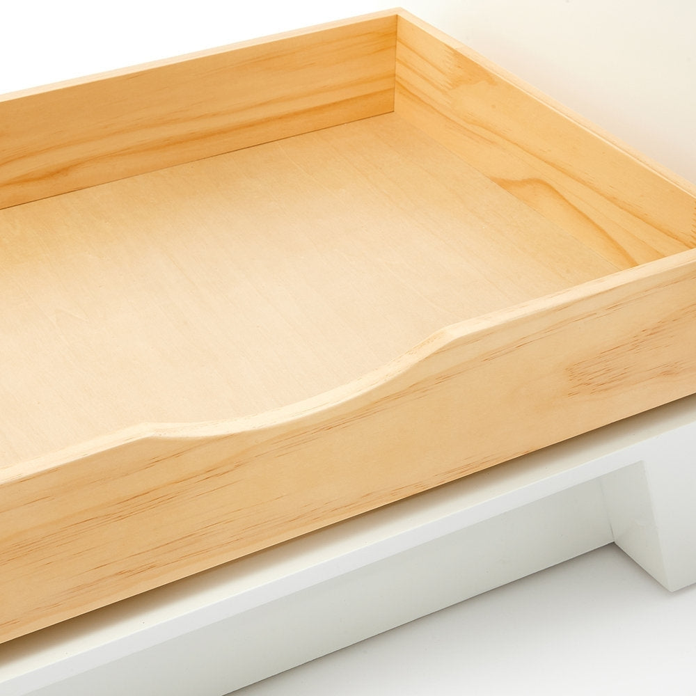 Close-up of a light natural solid wood drawer interior with visible grain and a curved front cutout, shown resting on the white base of a modern bathroom vanity.
