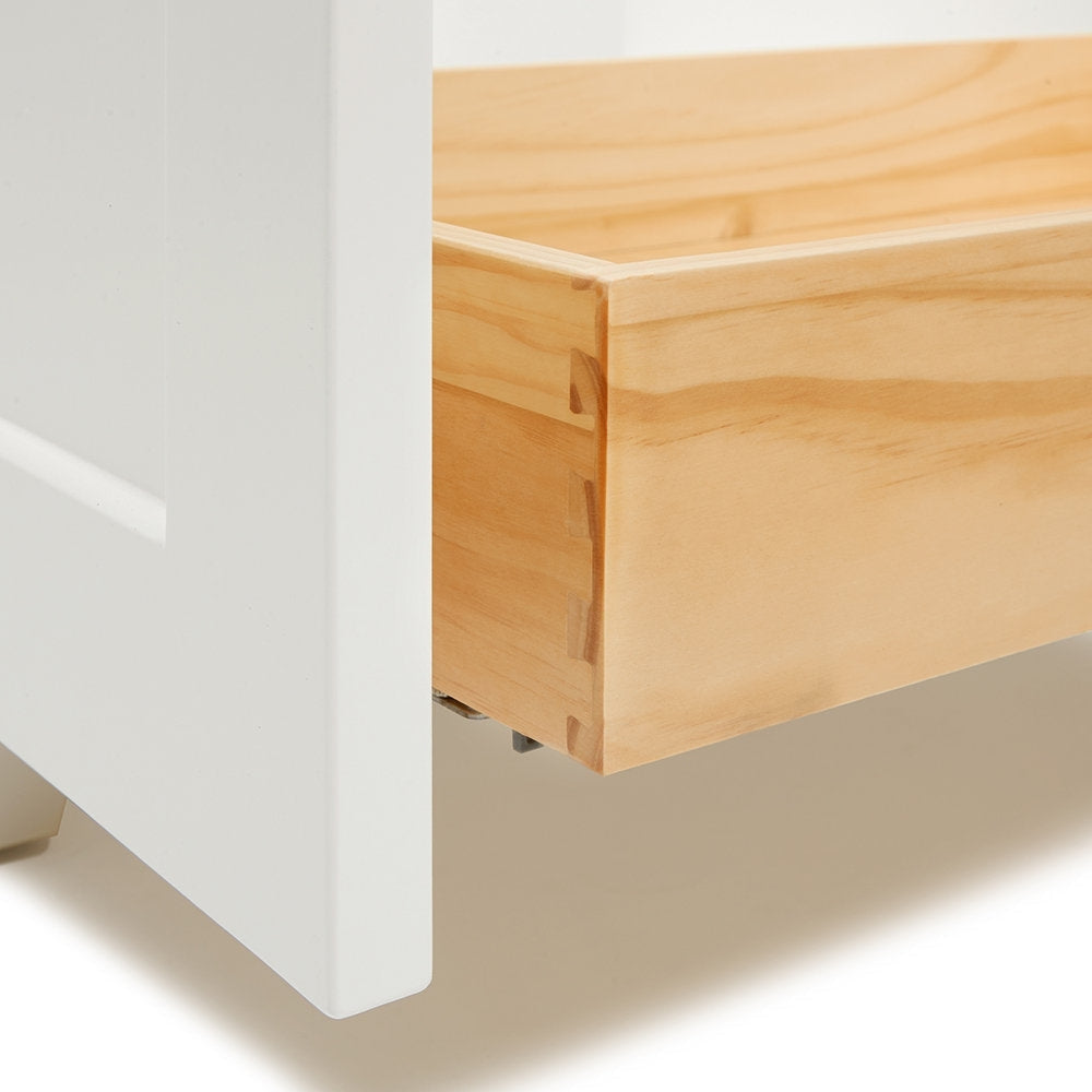 Close-up of a solid wood vanity drawer corner showing dovetail joinery, natural wood grain and the metal slide, positioned next to a white painted vanity front.