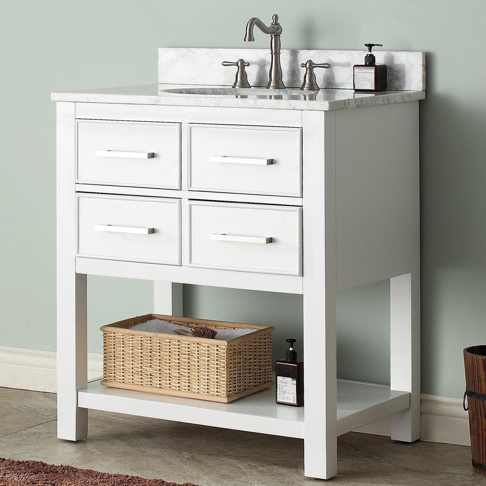 Modern solid wood bathroom vanity in stone finish with stone top and integrated ceramic sink, brushed nickel faucet, four front drawers with horizontal pulls and open lower shelf holding a wicker basket and soap dispenser.