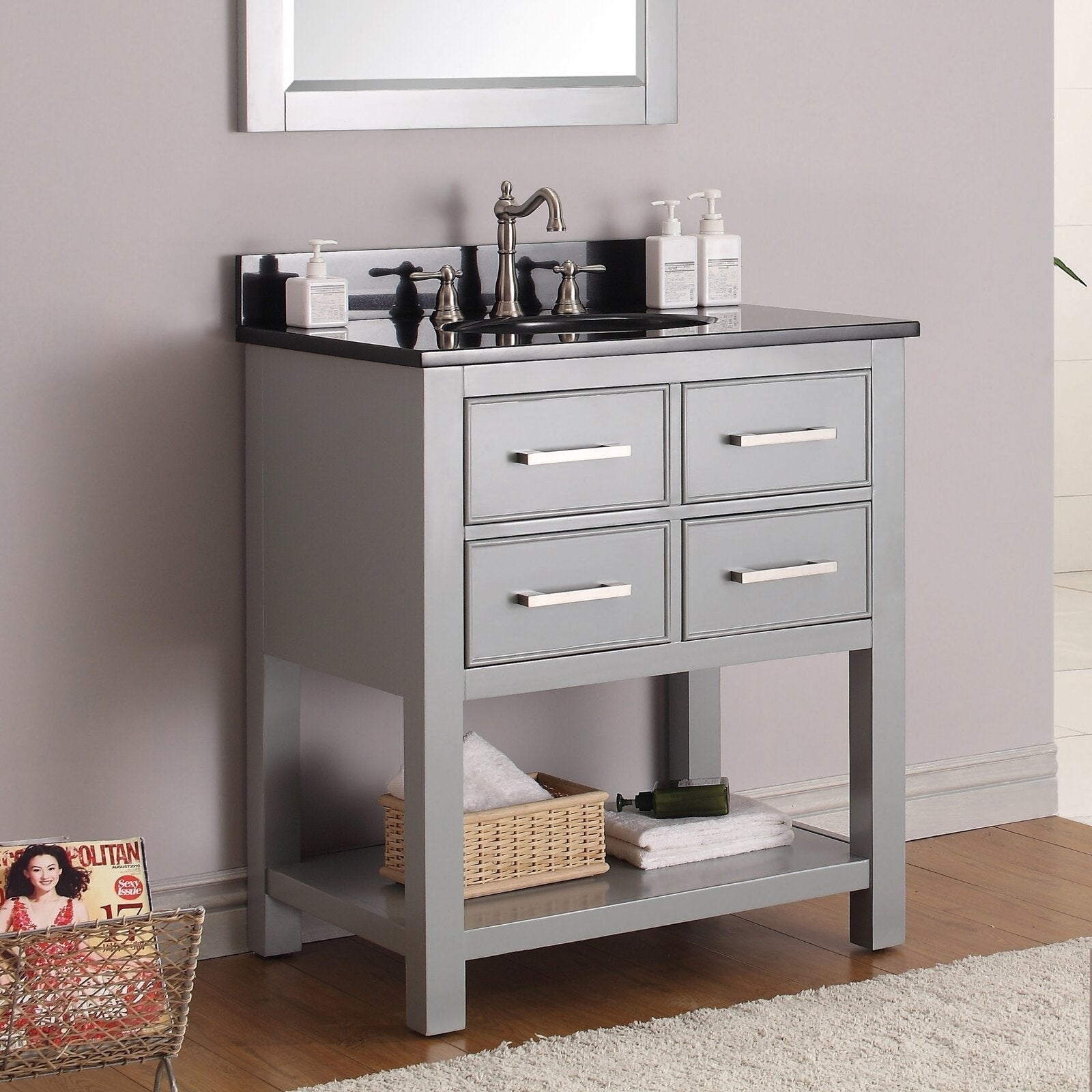 Modern solid-wood bathroom vanity in stone gray with a black stone countertop, single ceramic sink and brushed-nickel faucet, four drawers with metal bar handles and an open lower shelf with wicker basket and towels.