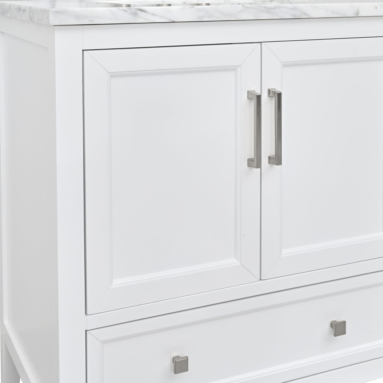 Close-up of a stone-topped modern white solid wood bathroom vanity showing two inset paneled doors with brushed nickel bar handles and a lower drawer with square metal knobs.