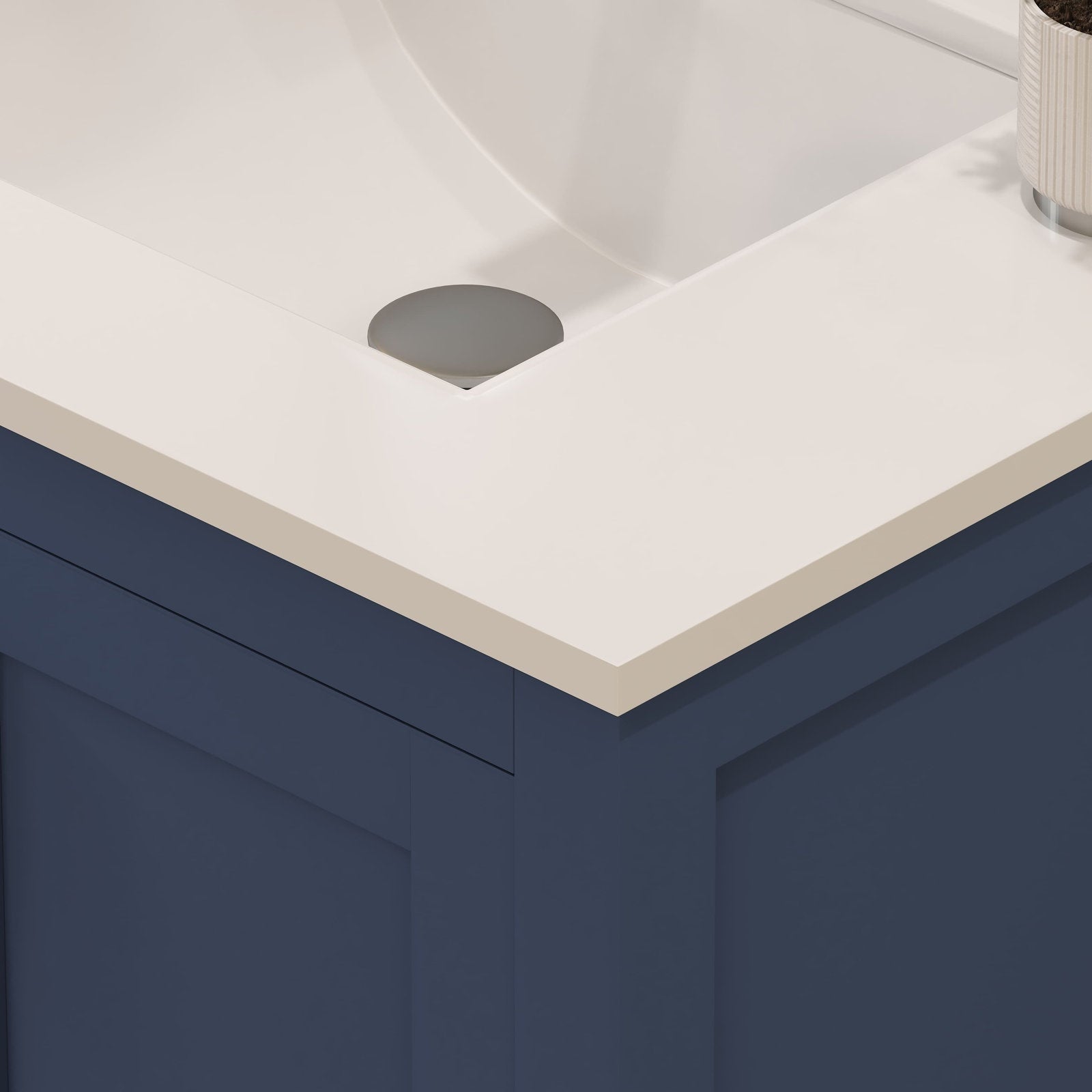 Close-up of a stone-colored top with an integrated ceramic sink and gray drain cap on a navy blue solid-wood modern vanity corner, showing the clean straight edge and recessed panel cabinet detail.