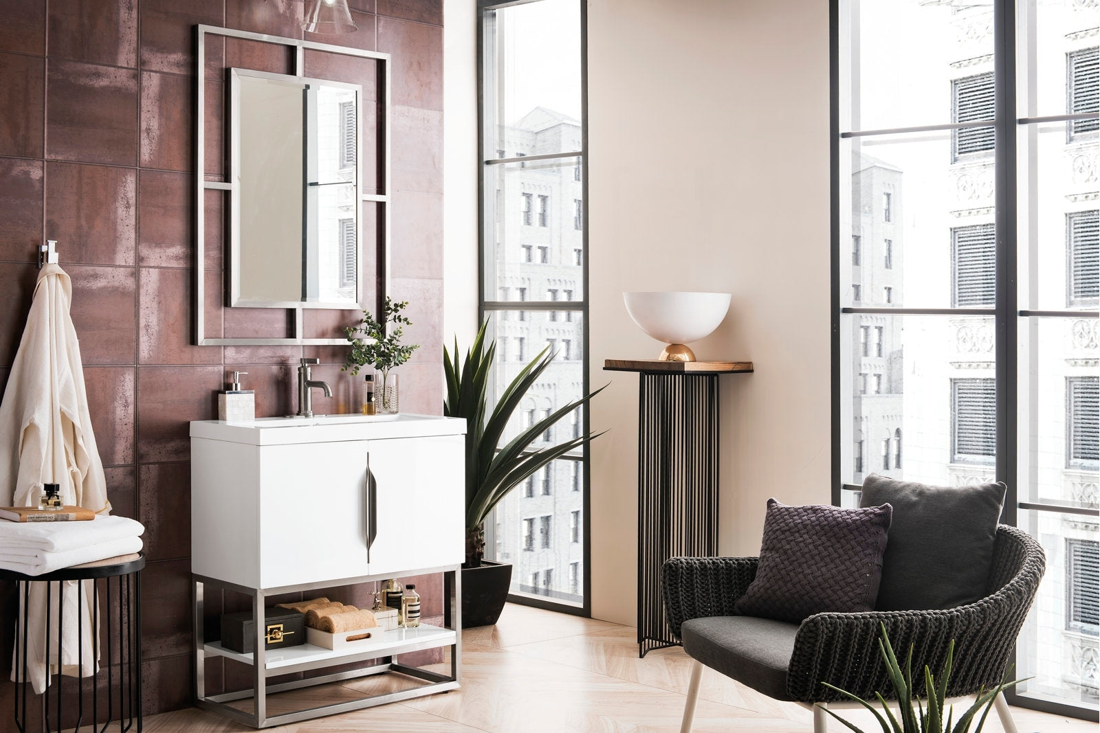 White freestanding single-sink vanity in solid wood with a stone countertop and brushed metal base, shown with a chrome faucet, rectangular mirror, open shelf with towels and toiletries and plants in a contemporary bathroom.