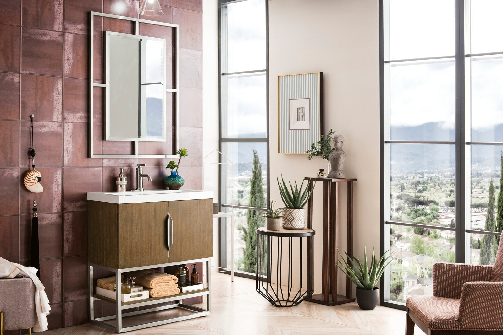 Modern contemporary freestanding single-sink bathroom vanity in solid wood with a white stone top and metal base, styled with a rectangular mirror, folded towels, potted plants and decorative accents by tall windows.