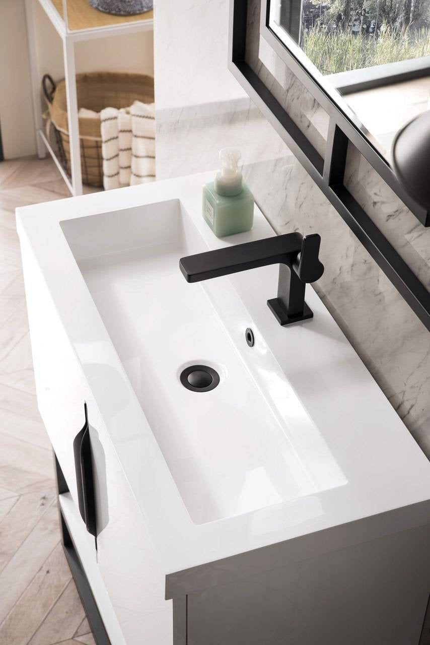Overhead view of a modern single-sink bathroom vanity with a white integrated stone countertop sink, matte black single-handle faucet and drain, black cabinet handle and solid wood base against a marble backsplash.