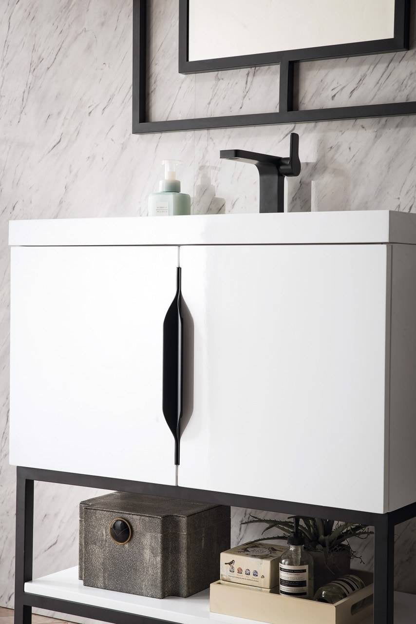 Close-up of a modern 31.5-inch white wooden freestanding bathroom vanity with stone-look marble backsplash, matte black faucet and elongated black cabinet handle; open lower shelf holds a storage box and toiletries.