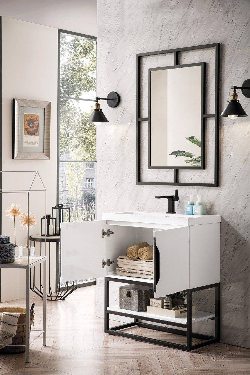 Freestanding modern single-sink bathroom vanity with a stone white top and glossy white cabinet on a black metal base; one door open to show folded towels and a lower shelf, paired with a black-framed mirror and matte black faucet.