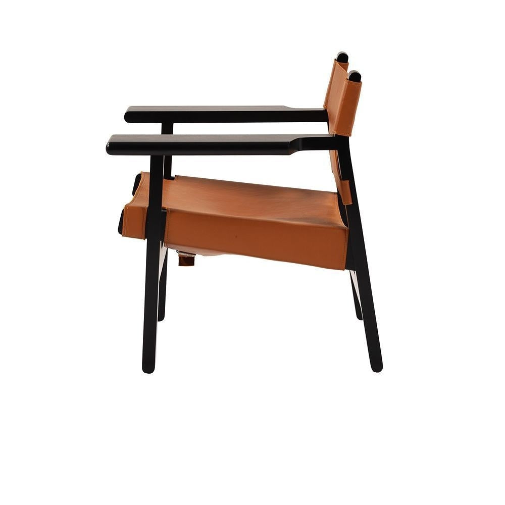 Side view of a modern lounge chair with a black solid wood frame and tan leather sling seat and back, featuring straight armrests and minimalist angled legs.