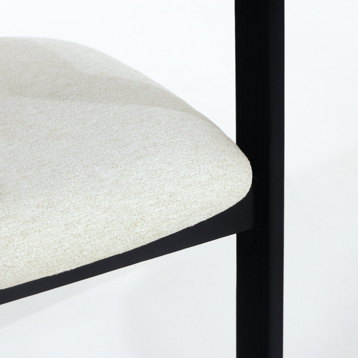 Close-up of a beige boucle upholstered dining chair seat showing the rounded cushioned edge and a slim black frame leg against a white background.