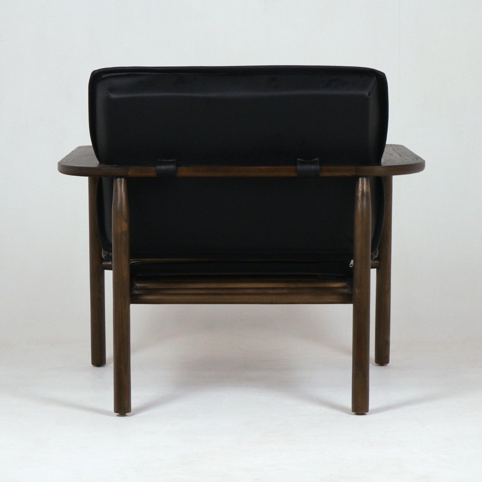 Rear view of a mid-century modern lounge chair with a black faux leather low back cushion secured by straps to a dark stained solid wood frame, rounded legs, and wide flat wooden armrests.