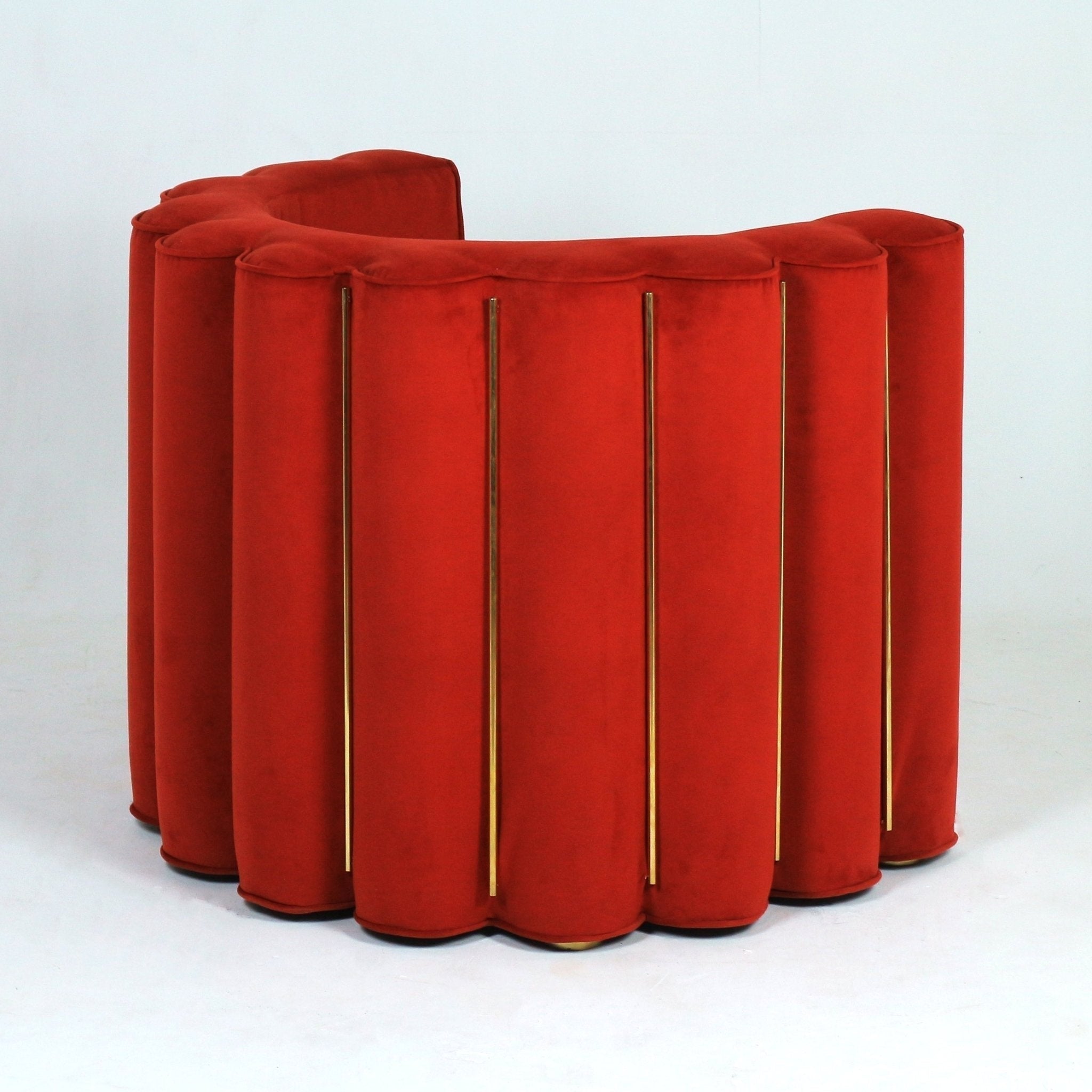 Modern red velvet upholstered accent chair with a scalloped curved back, vertical slim gold metal accents between padded channels and a low wooden base, shown on a white studio background.