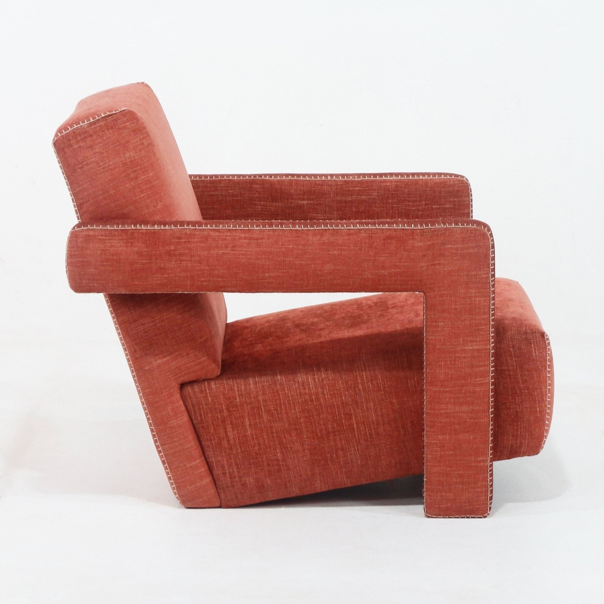 Side profile of a modern fabric-upholstered lounge chair in rust red, featuring a geometric open rectangular arm, full back and visible white contrast topstitching along the edges.