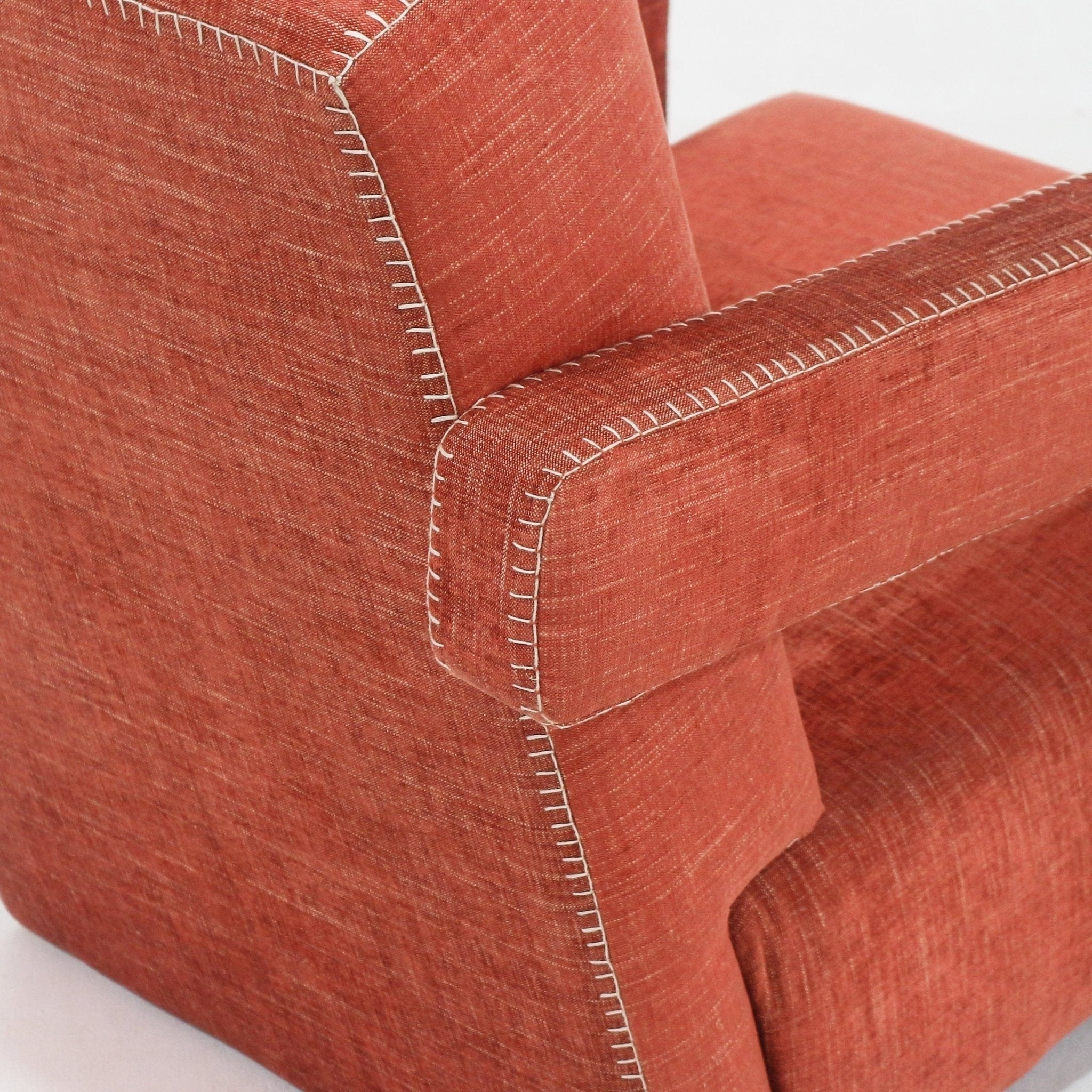 Close-up of a fabric-upholstered lounge chair arm and back corner, highlighting white contrast whipstitching and textured woven fabric on a modern contemporary accent chair.
