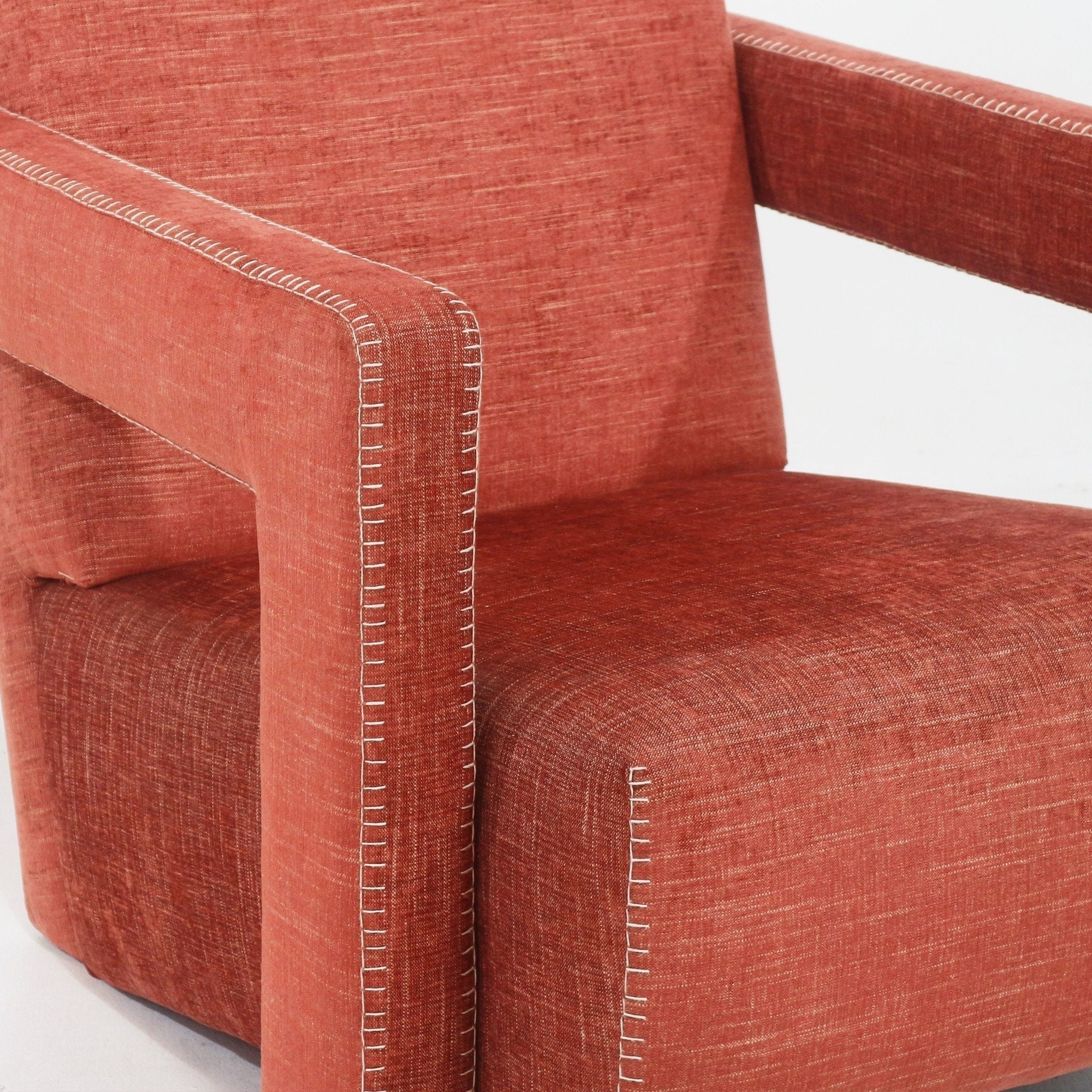 Close-up of a cabernet-red fabric-upholstered modern lounge chair showing the squared arm, cushioned seat and white contrast blanket-stitch detailing along the seams.