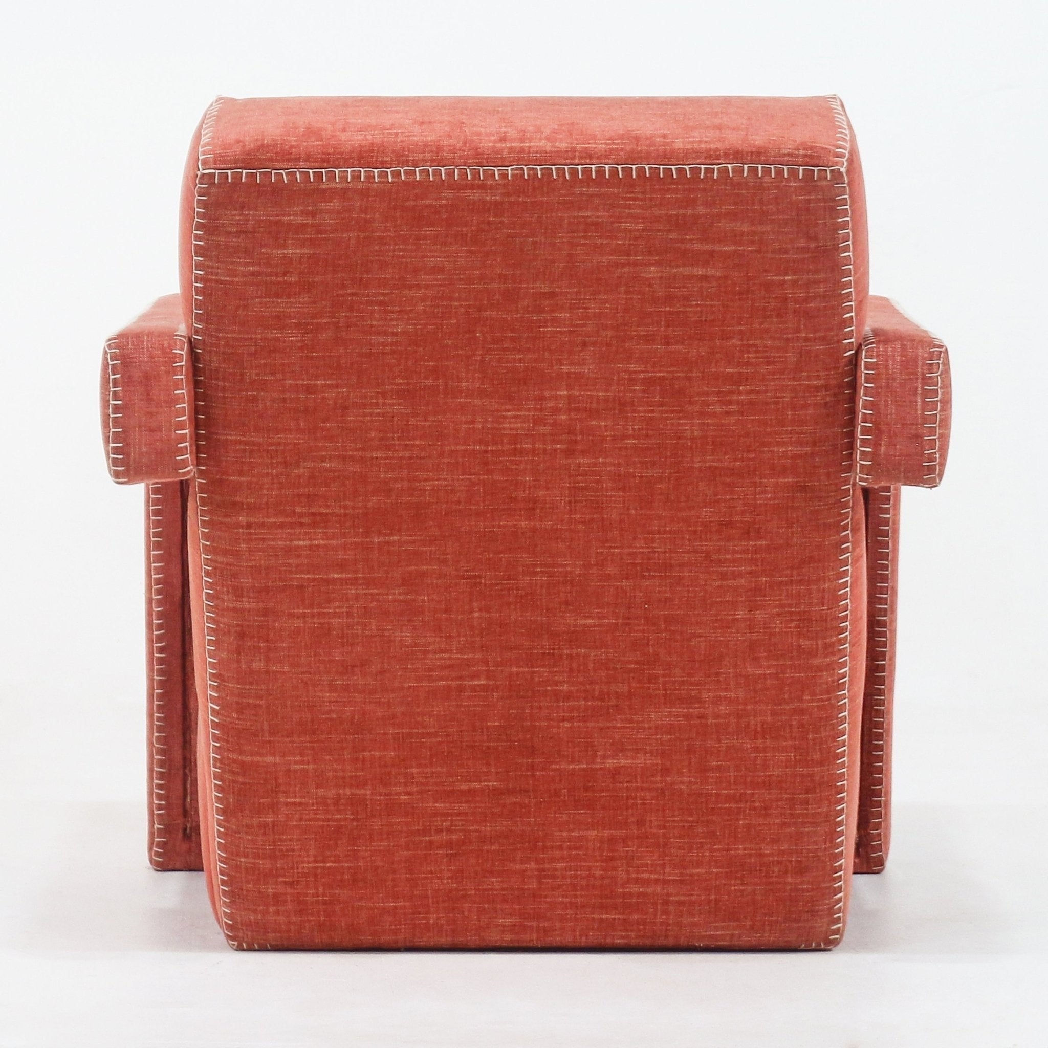 Back view of a modern fabric-upholstered accent chair in warm terracotta red with white contrast whipstitching along the edges and squared armrests.