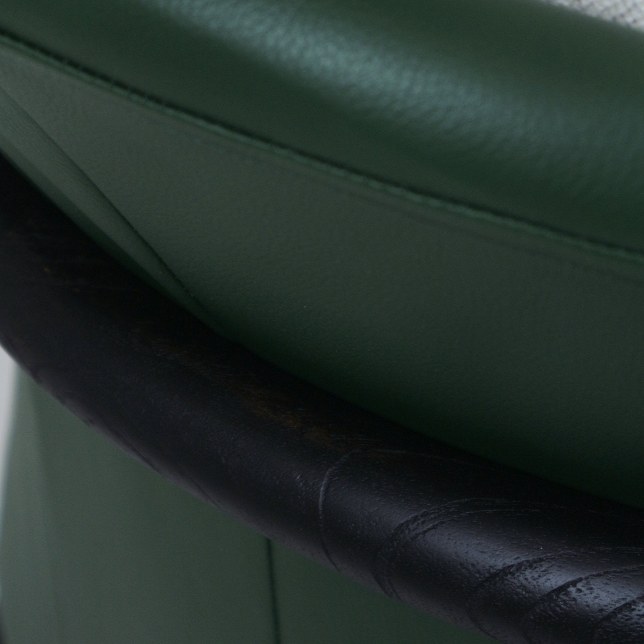 Close-up of green leather seat cushion and a dark-stained teak armrest showing stitched detailing and subtle wood grain on a mid-century modern arm chair.