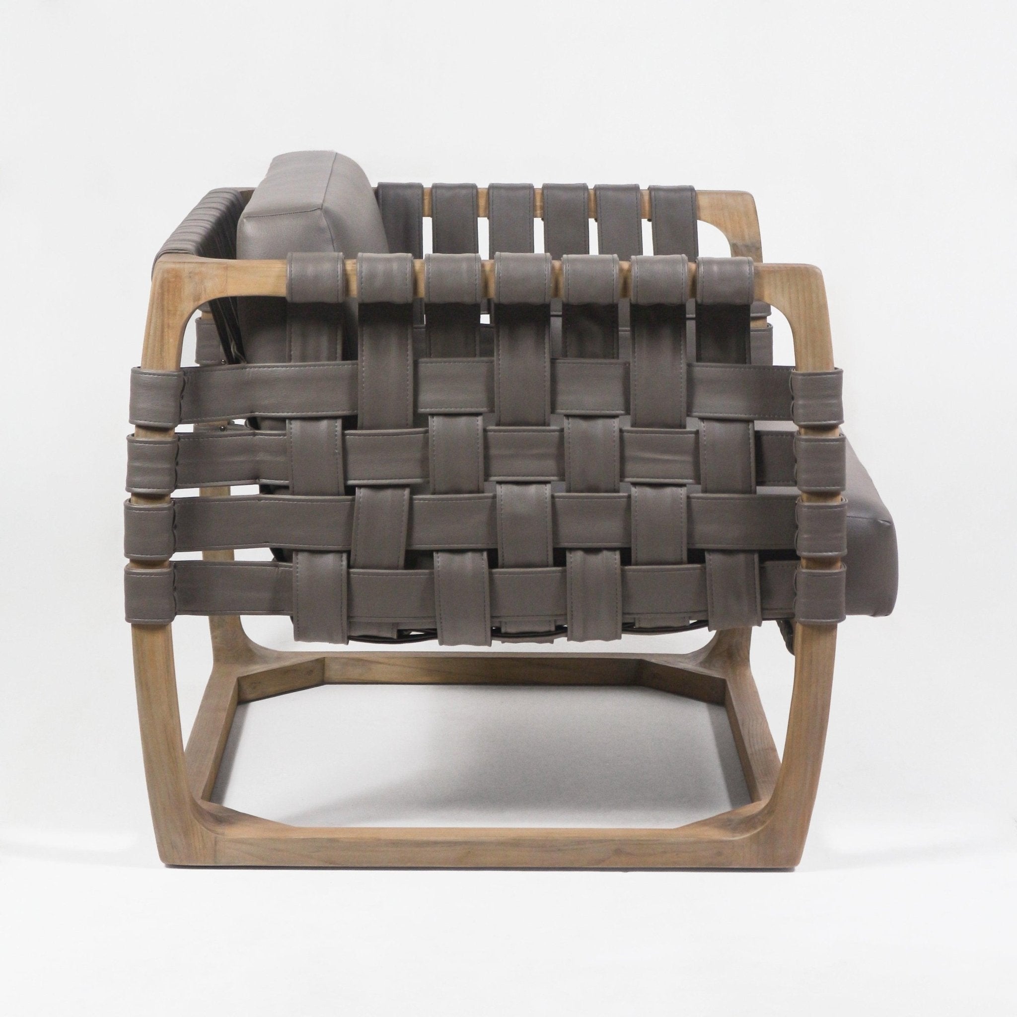 Side view of a modern webbed lounge chair with a natural solid wood frame and wide dark brown leather straps woven across the sides and back, plus a matching cushioned low-profile seat.