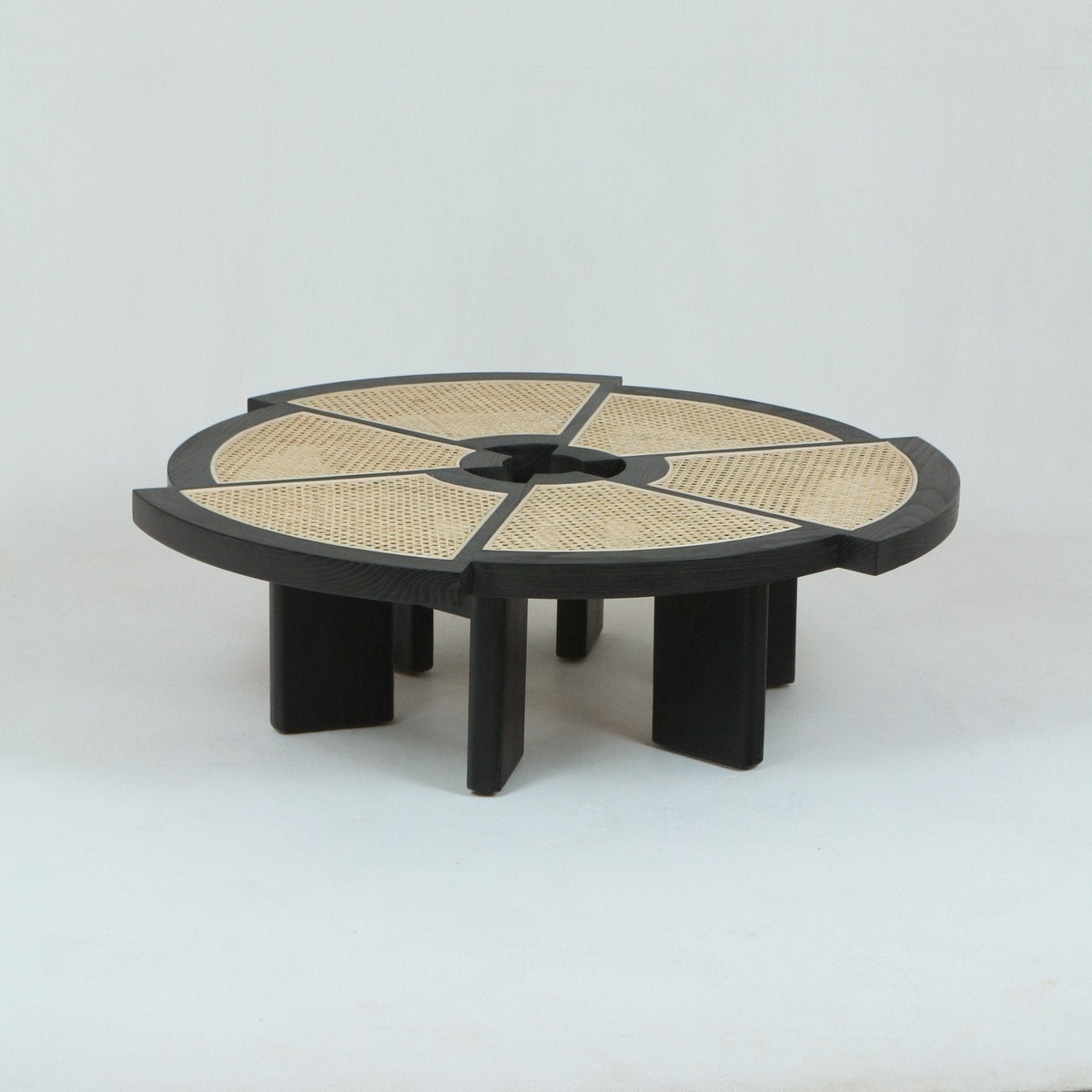 Low round modern coffee table in natural oak with six short rectangular legs and woven cane inset panels arranged in radial segments around a central circular opening.