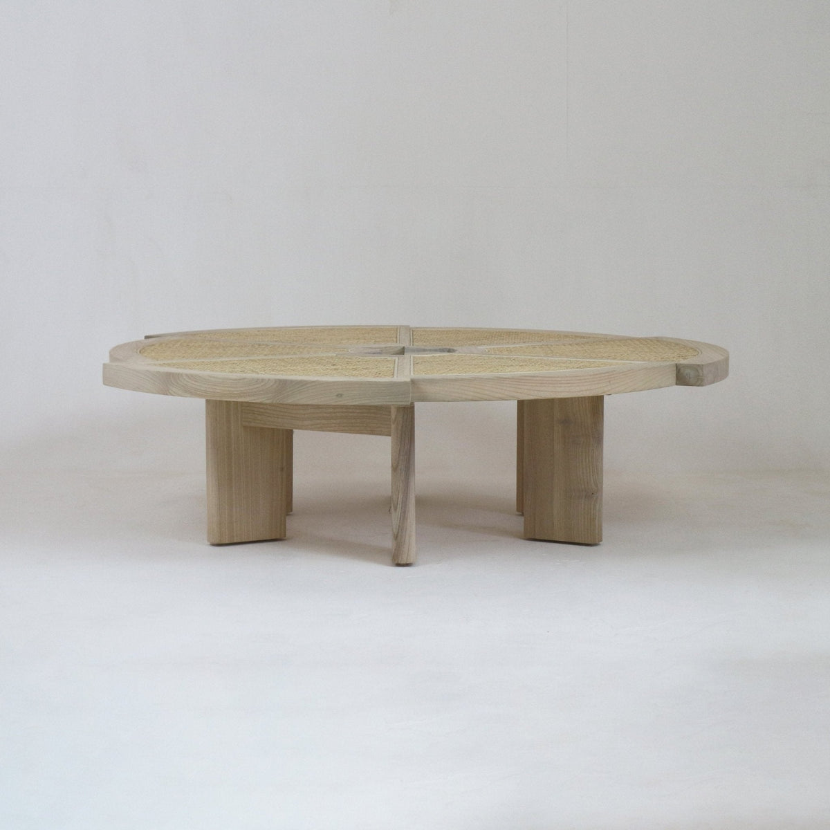 Low round coffee table in natural oak with a woven cane inset top divided into four quadrants and four chunky rectangular legs, shown against a neutral studio background.