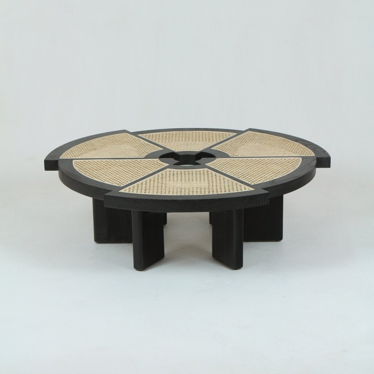 Low round coffee table with a dark solid wood (oak) frame and segmented natural cane insets arranged around a central hub, supported by thick rectangular wood legs for a modern mid-century look.