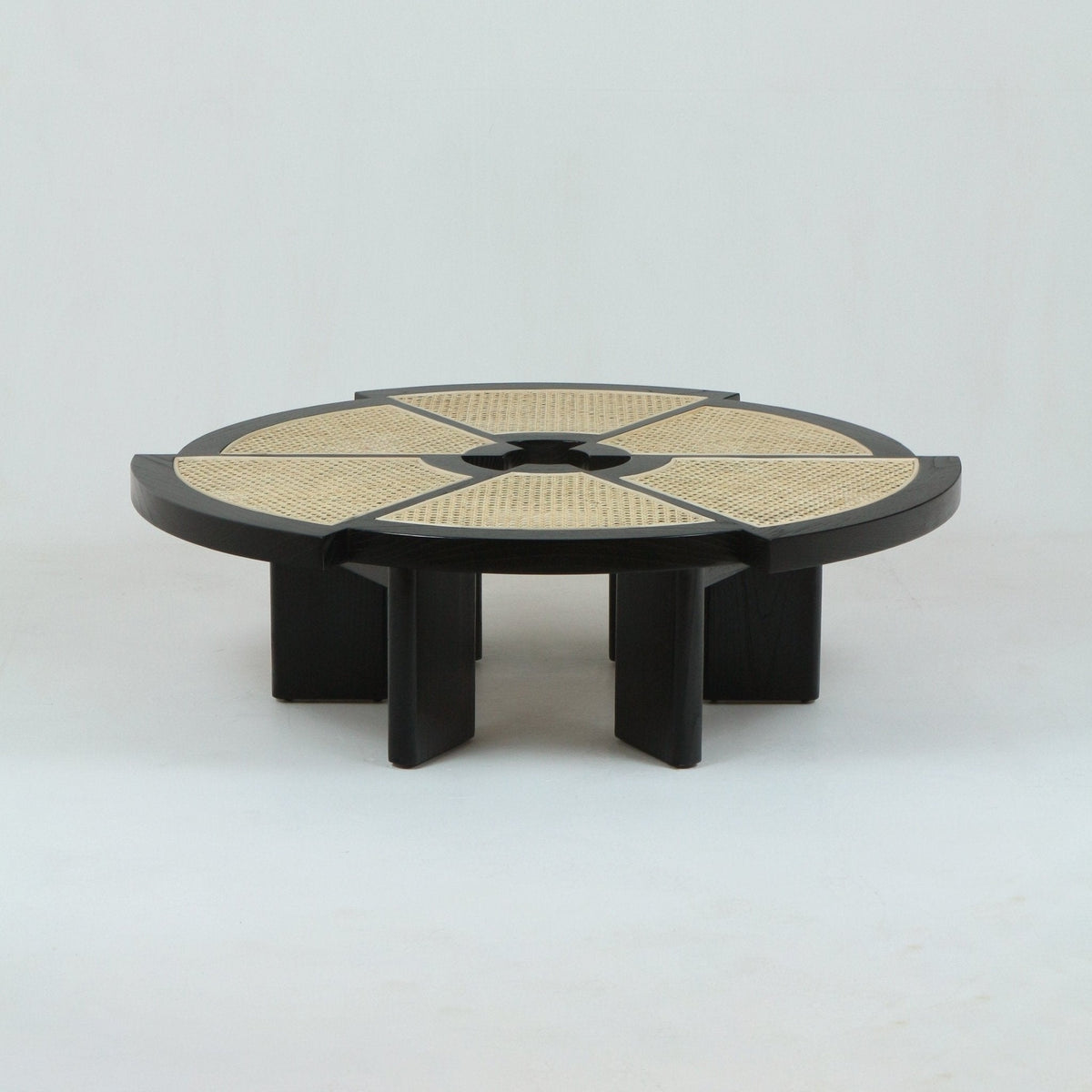 Low round coffee table with natural woven cane panels arranged in radial segments set into a dark-stained oak frame, featuring a central circular opening and short chunky black wood legs.