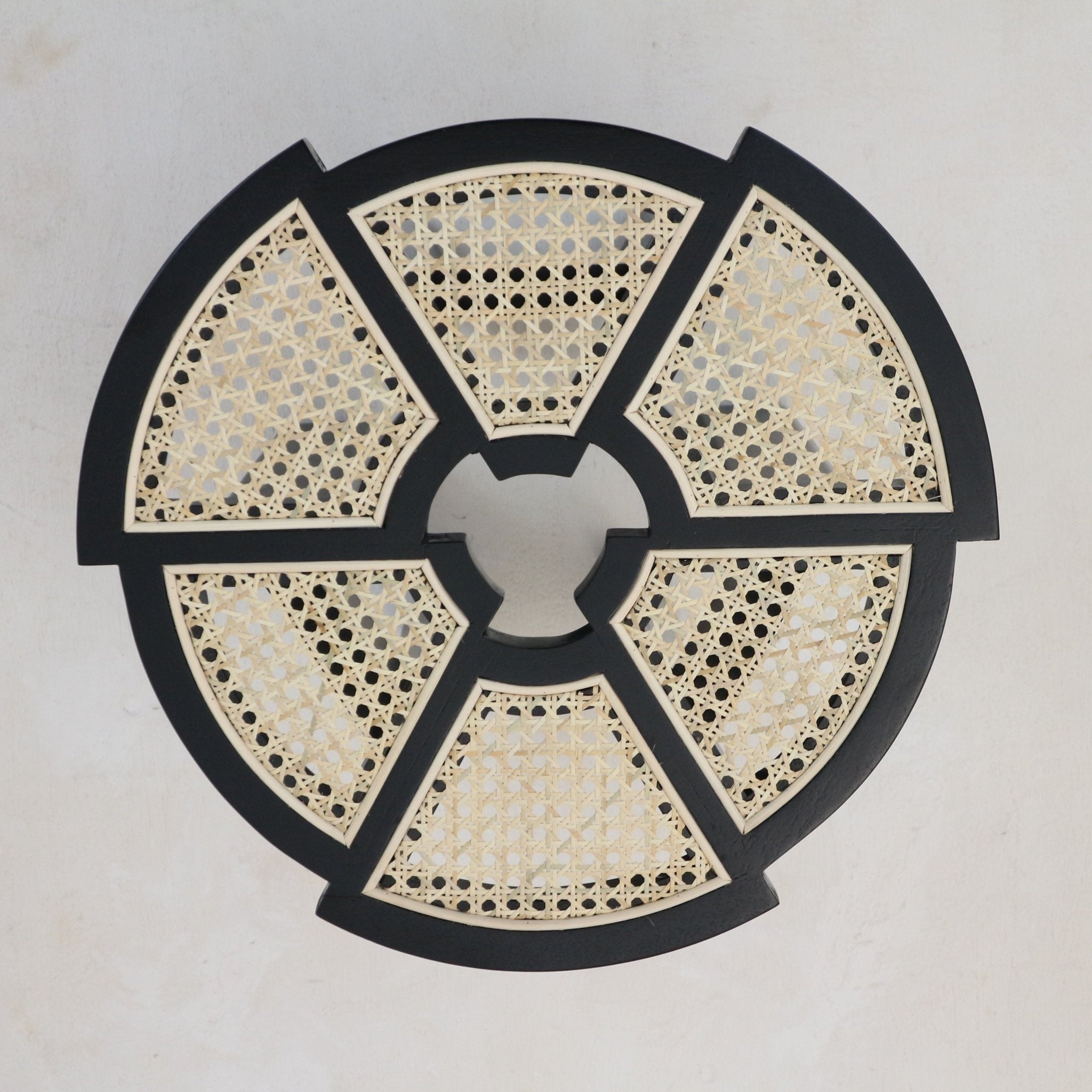 Top-down view of a round black gloss solid-wood side table top featuring six natural rattan cane panels arranged in a segmented wheel pattern.