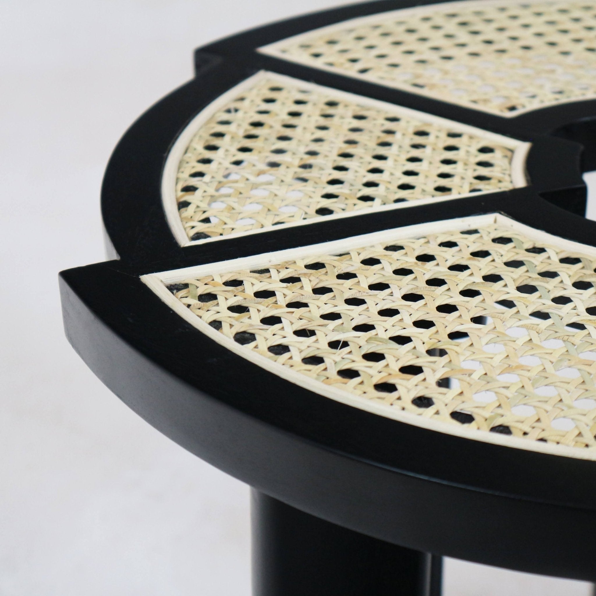 Close-up of a black gloss solid wood side table top with natural cane rattan inlay, highlighting the woven cane pattern and curved segmented black frame in a modern mid-century style.