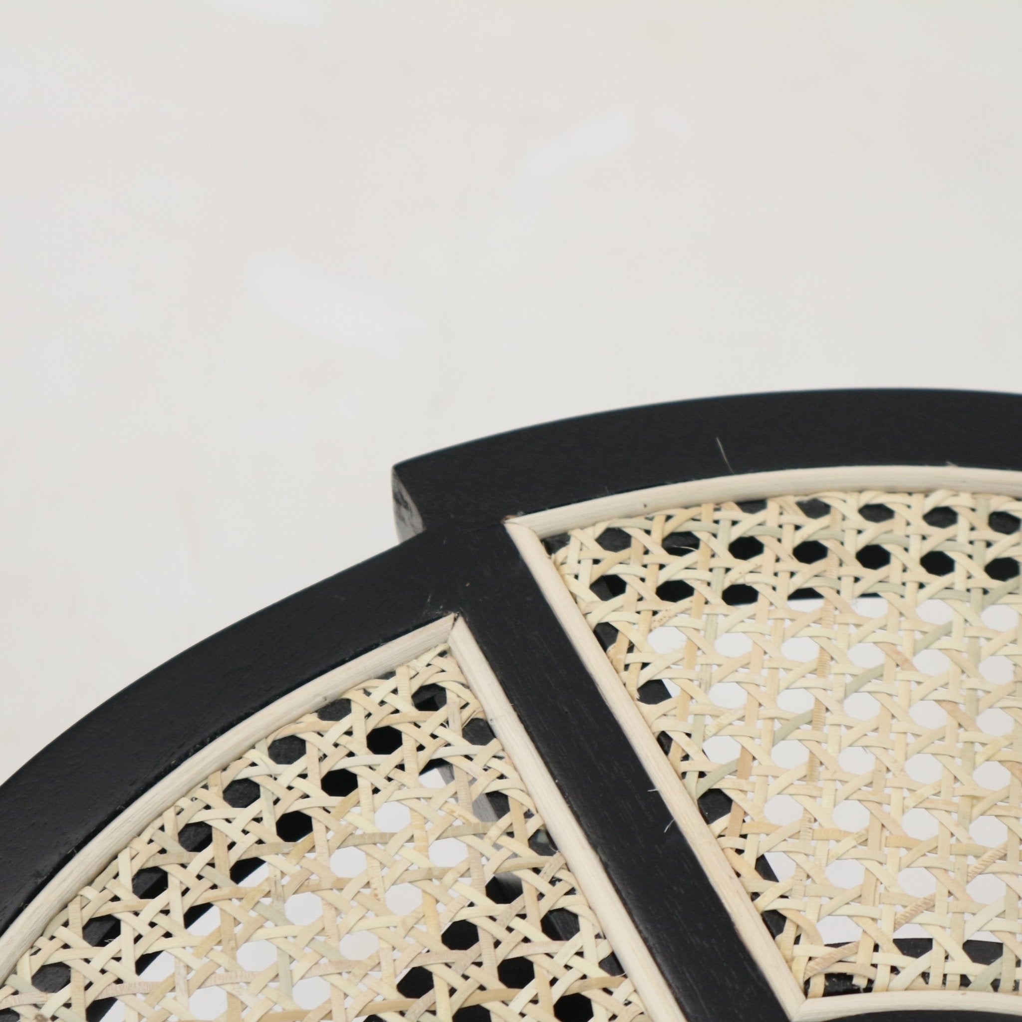 Close-up of a black-gloss wooden side table top with a natural cane rattan inset, showing the intersecting black crossbar and framed natural rattan edging.