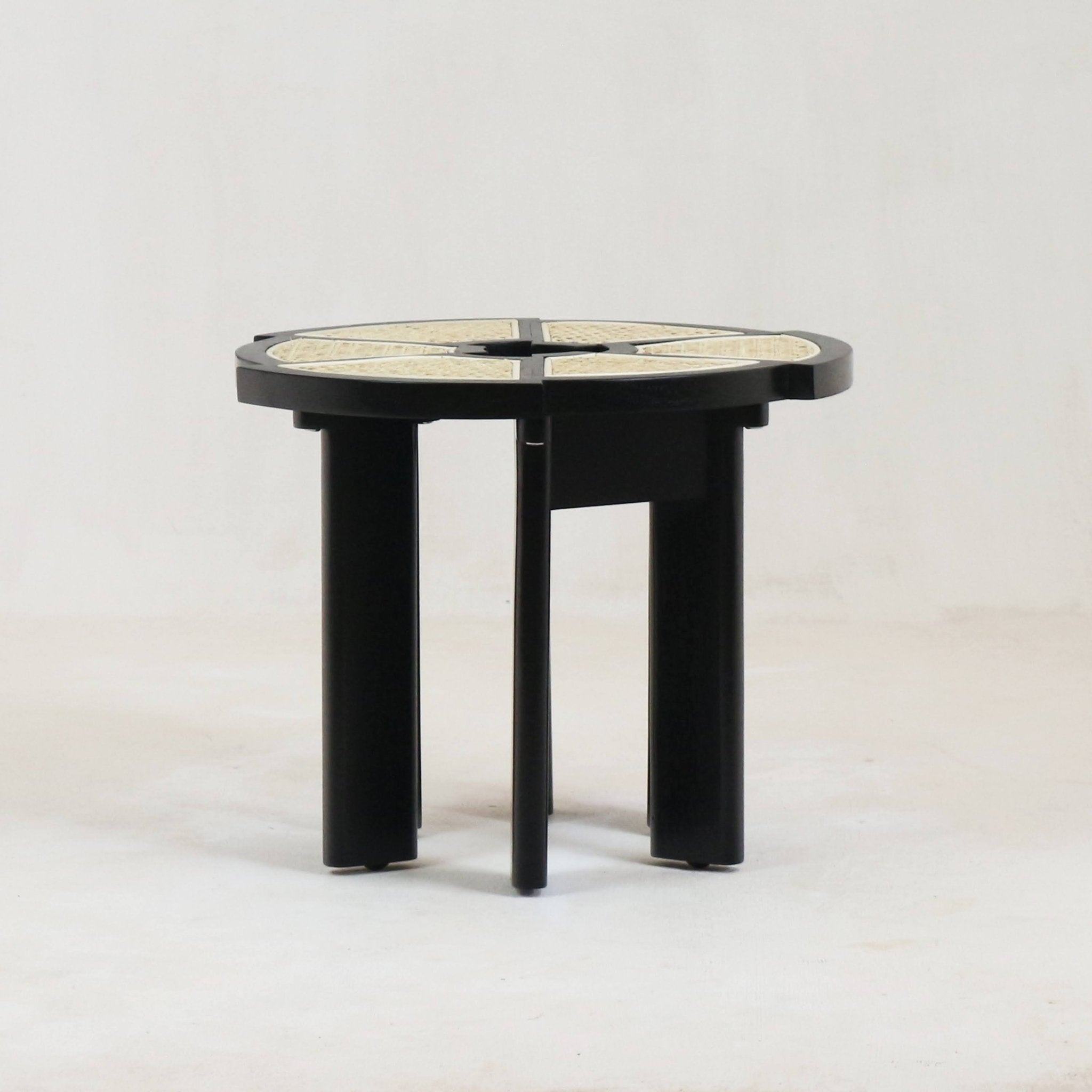 Round black-gloss wooden side table with a natural cane inset top divided into four wedge panels and four thick vertical legs, modern mid-century style.